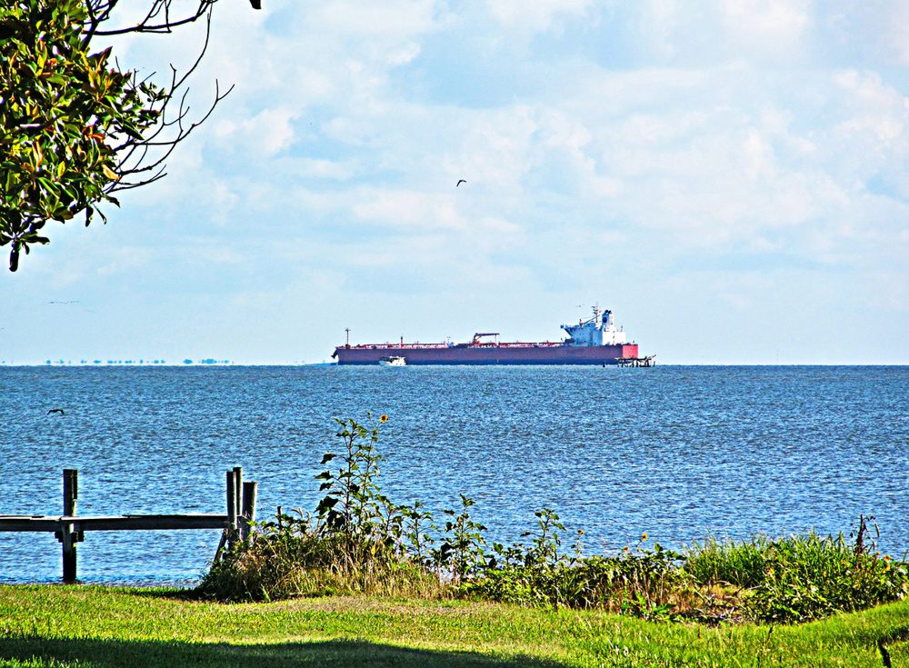 Orange cargo ship with tugboat entering Houston Ship Channel from Gulf of Mexico